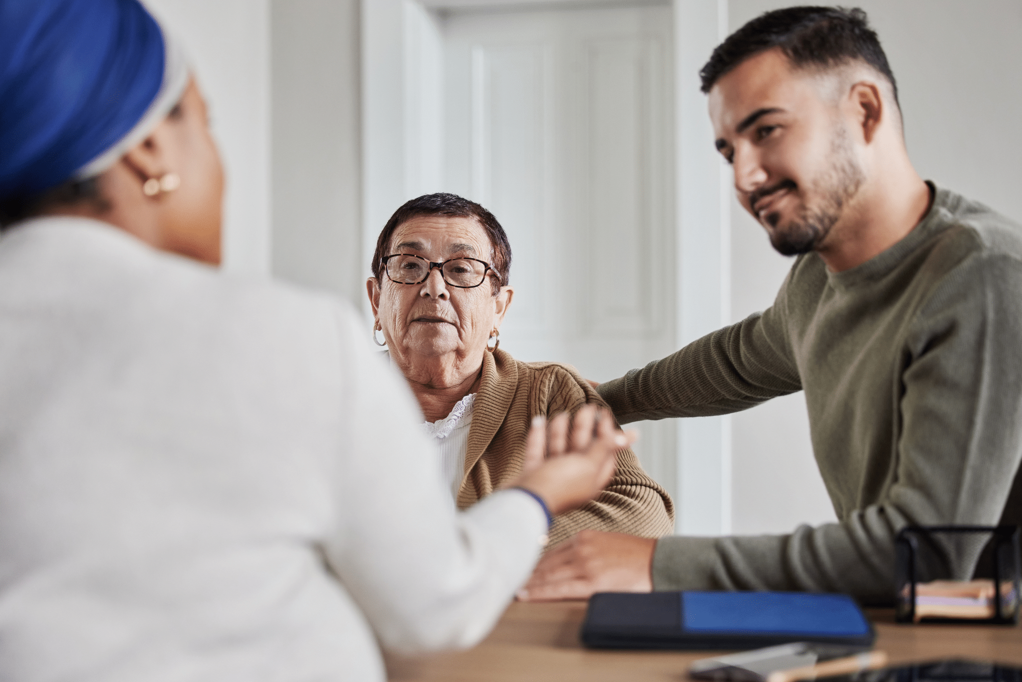 Young man holding the hand of an elderly man during a conversation with a woman in a blue headscarf at a table. Young man holding the hand of an elderly man during a conversation with a woman in a blue headscarf at a table.